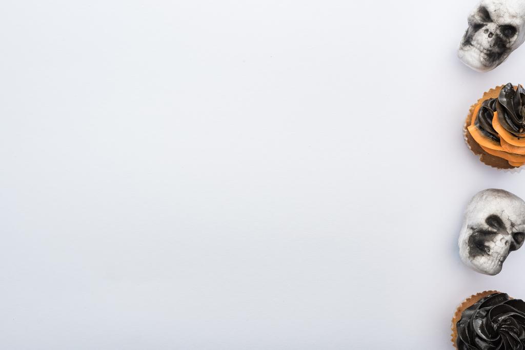 Κορυφαία θέα από νόστιμα κεκάκια αποκριών με κρανία σε λευκό φόντο με χώρο αντιγραφής - Φωτογραφία, εικόνα