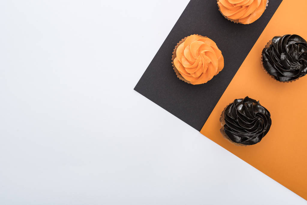 Top uitzicht van heerlijke Halloween cupcakes op zwart, oranje en witte achtergrond met Kopieer ruimte - Foto, afbeelding