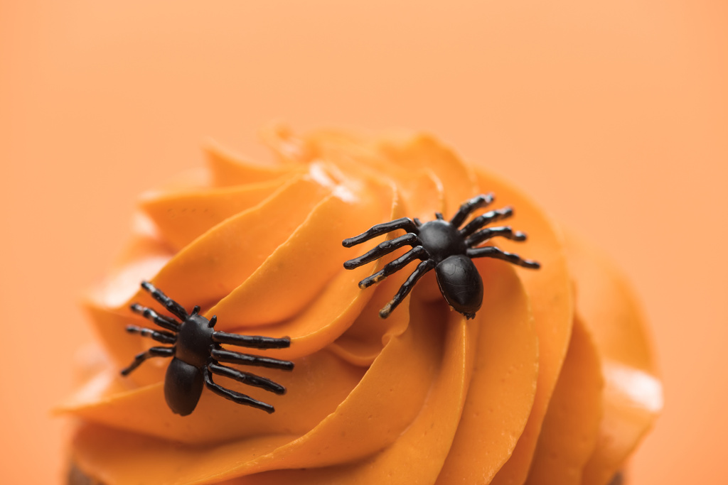 close up view of spooky Halloween cupcake with spiders on cream isolated on orange - Photo, Image