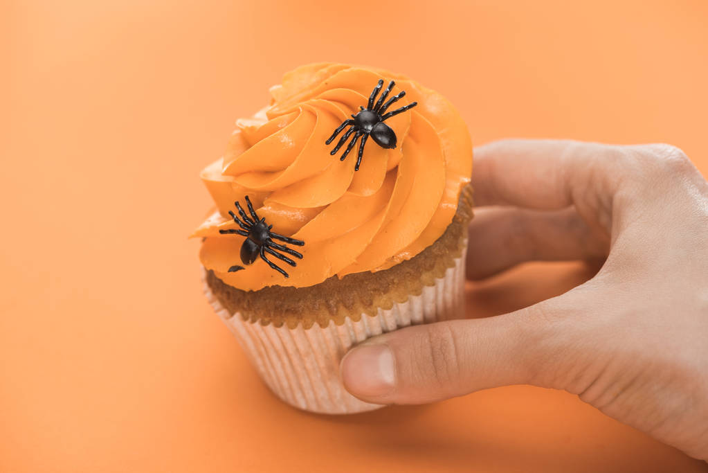 cropped view of woman holding delicious Halloween cupcake with spiders on orange background - Photo, Image
