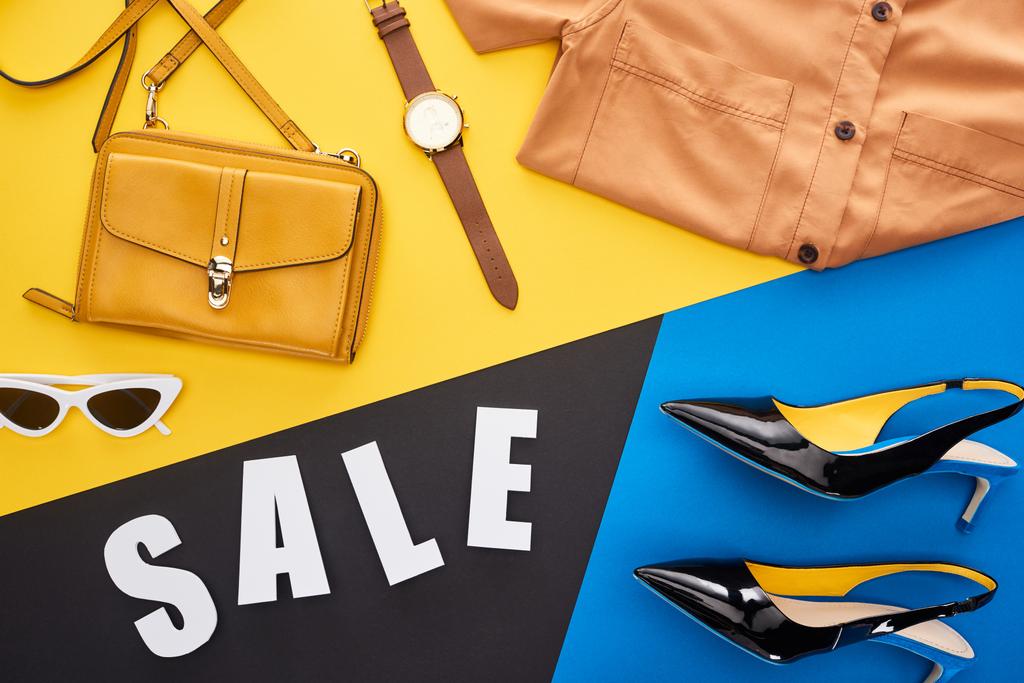 bovenaanzicht van verkoop belettering in de buurt van modieuze kleding op blauwe, gele en zwarte achtergrond - Foto, afbeelding