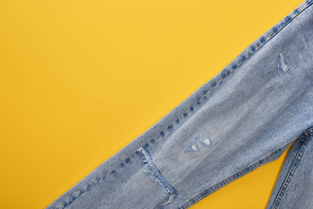 黄色を背景にしたファッショナブルなジーンズのトップビュー - 写真・画像
