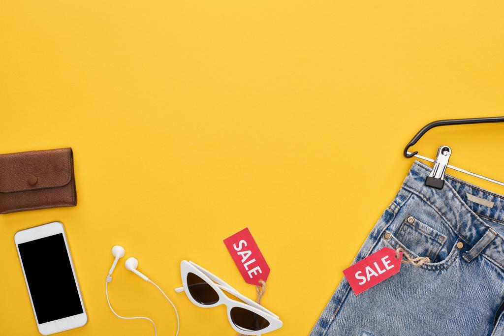 vista superior de ropa y accesorios de moda con etiquetas de teléfonos inteligentes y venta sobre fondo amarillo
 - Foto, imagen