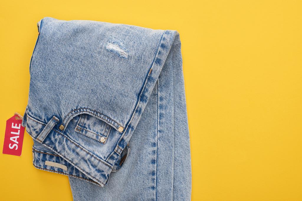 bovenaanzicht van jeans met sale label op gele achtergrond - Foto, afbeelding