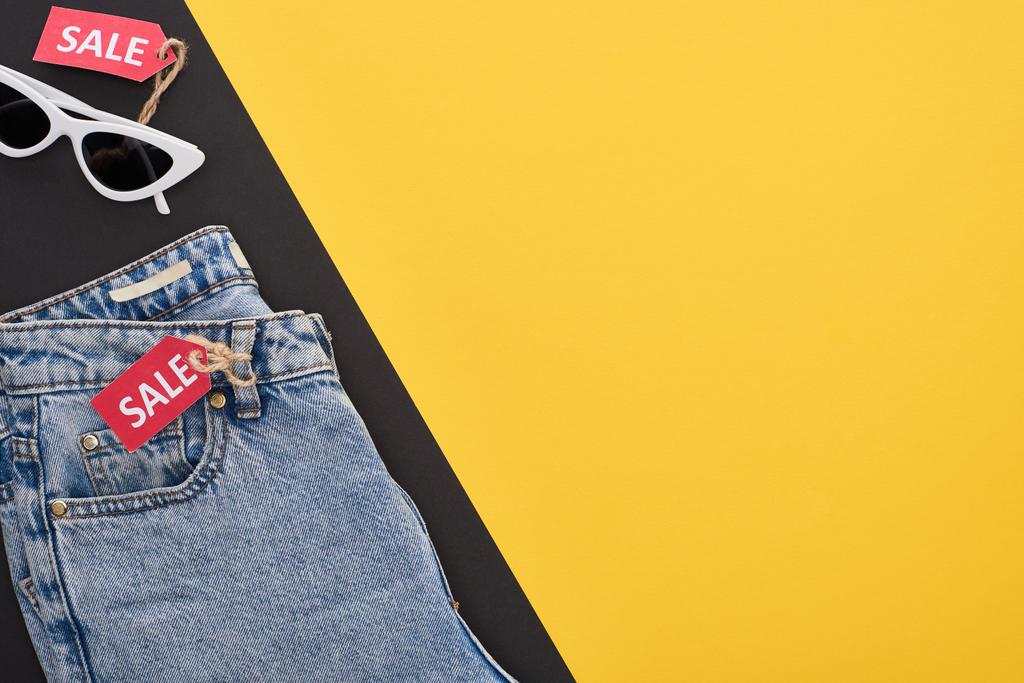 黄色と黒の背景に販売ラベルのあるジーンズと眼鏡のトップビュー - 写真・画像