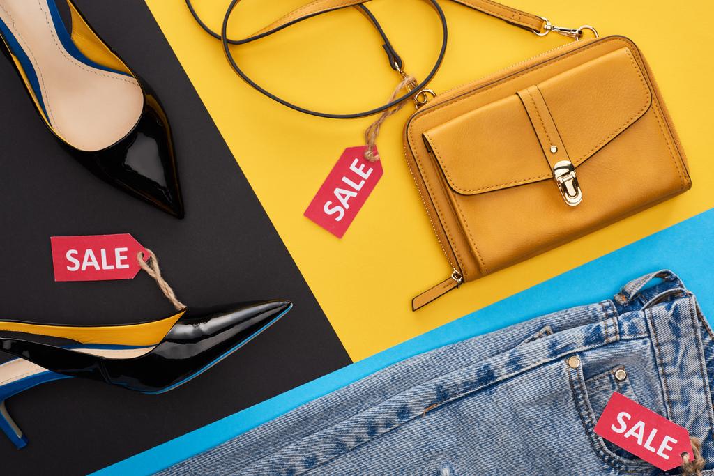 vrchní pohled na džíny, boty a tašku s prodejními etiketami na modrém, žlutém a černém pozadí - Fotografie, Obrázek