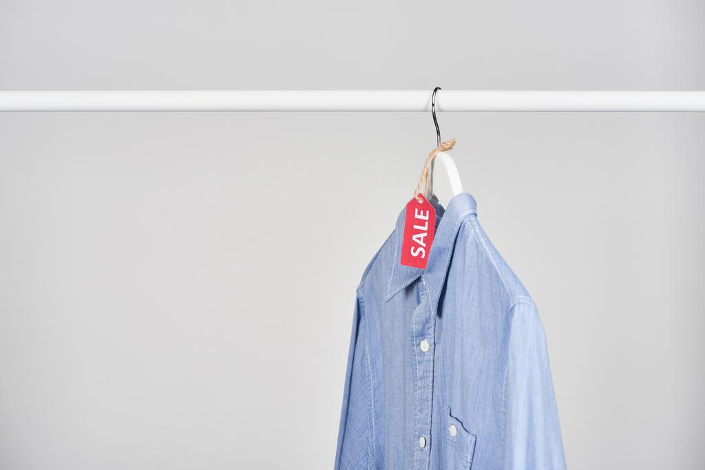 camisa azul colgando con etiqueta de venta aislada en blanco
 - Foto, imagen