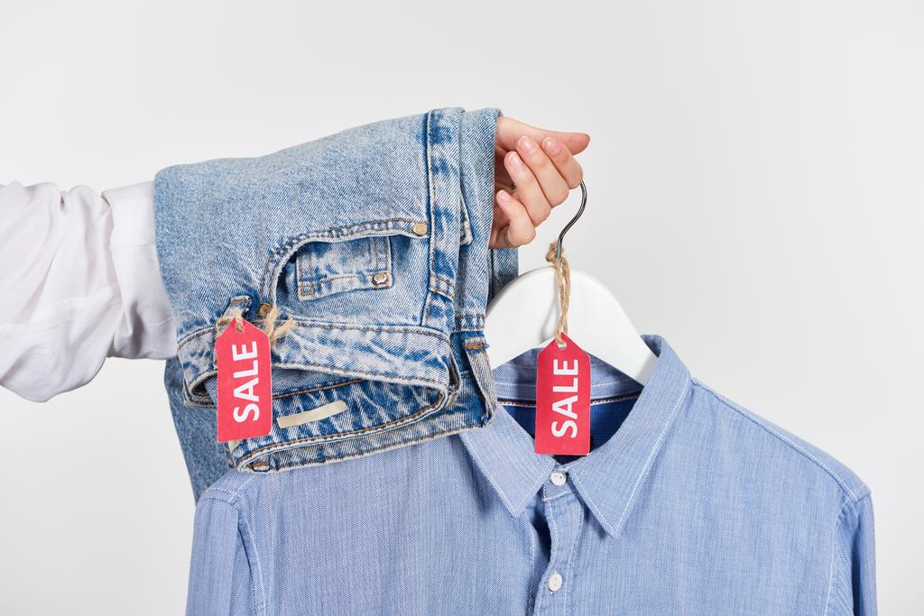 vista recortada de mujer sosteniendo jeans y camisa con etiquetas de venta aisladas en blanco
 - Foto, Imagen