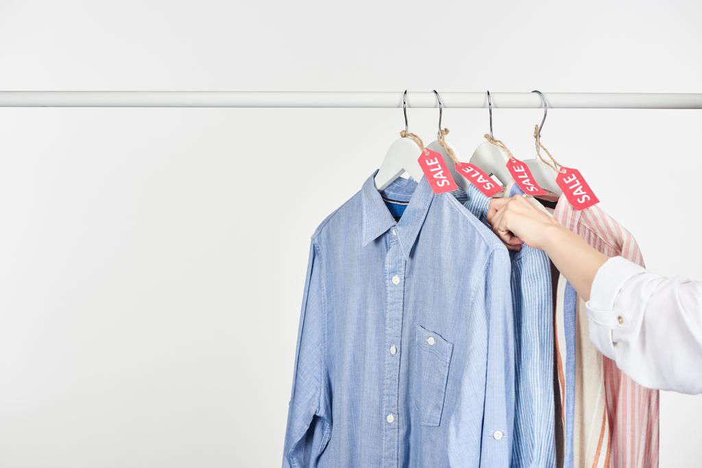 vista ritagliata di donna vicino a camicie eleganti appese con etichette di vendita isolate su bianco
 - Foto, immagini