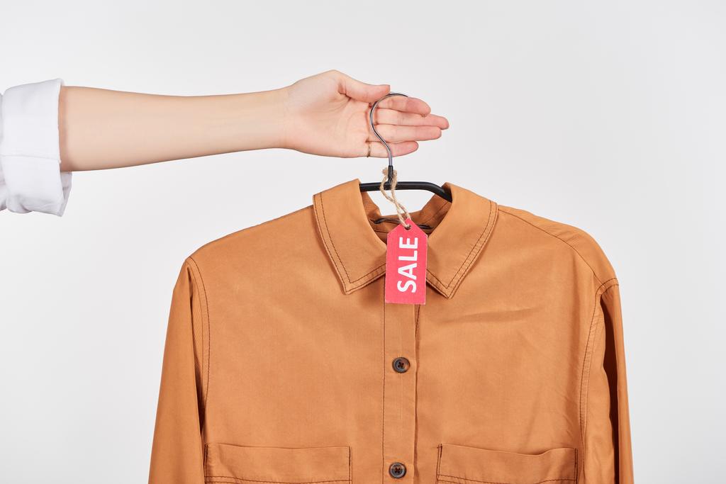 copped view of woman holding brown elegant shirt with sale labels isolated on white - Photo, Image