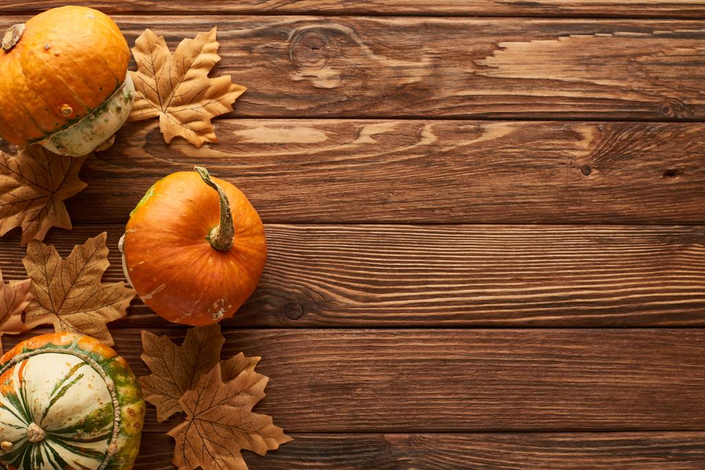 pohled na malé dýně na hnědém dřevěném povrchu se sušenými podzimními listy - Fotografie, Obrázek