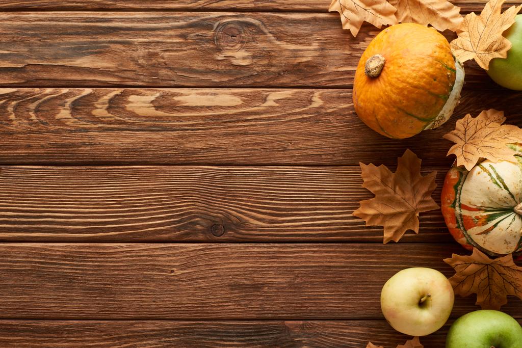 вид сверху на тыквы и яблоки на коричневой деревянной поверхности с сушеными осенними листьями и копировальным пространством
 - Фото, изображение