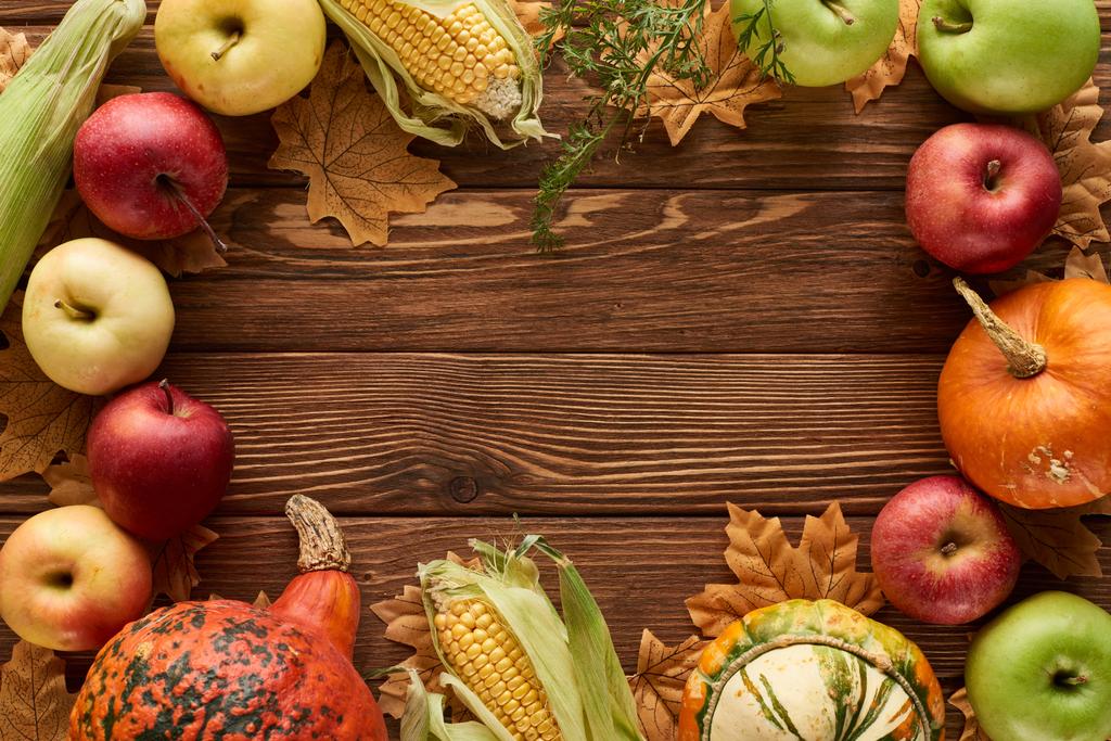 Widok z góry na ramie dynie, kukurydza słodka i jabłka na powierzchni drewnianej z suszonymi jesiennych liści - Zdjęcie, obraz