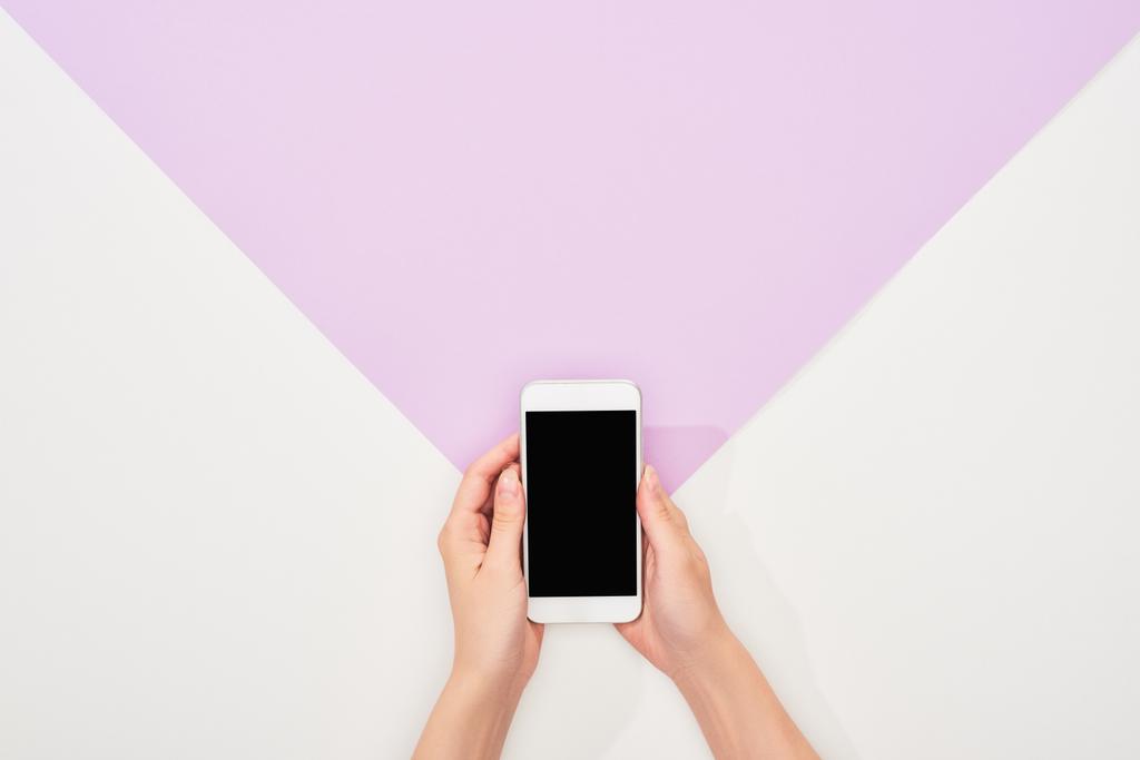 vista recortada de la mujer sosteniendo teléfono inteligente sobre fondo violeta y blanco
 - Foto, imagen