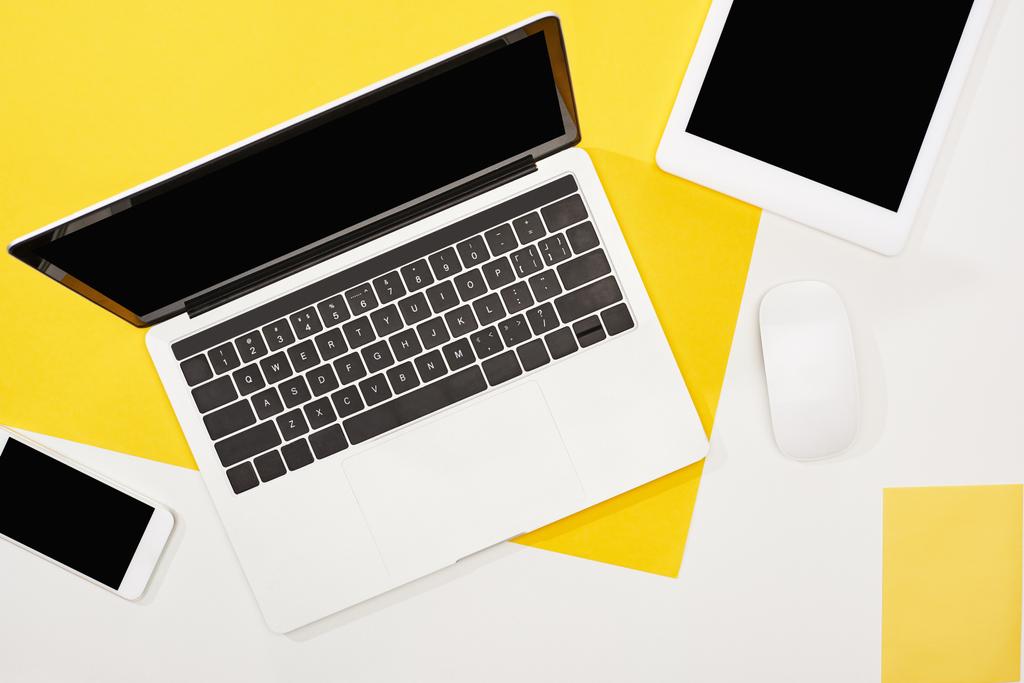 Top View van laptop, smartphone, digitale tablet met blanco scherm en computermuis op gele en witte achtergrond - Foto, afbeelding