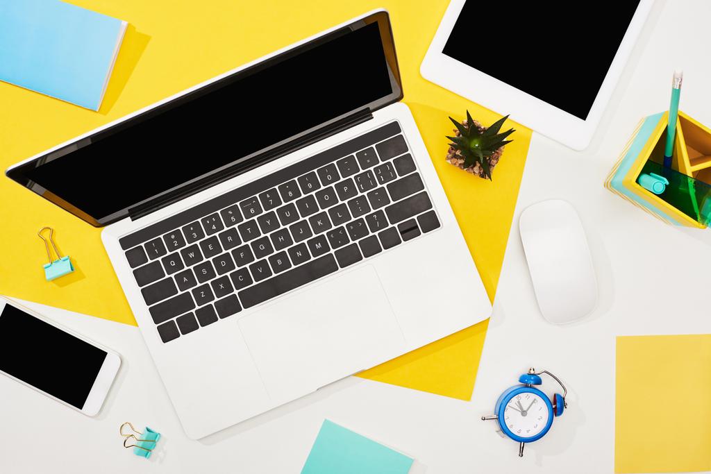 top view of laptop, smartphone, digital tablet with blank screen and computer mouse with office supplies on yellow and white background - Photo, Image