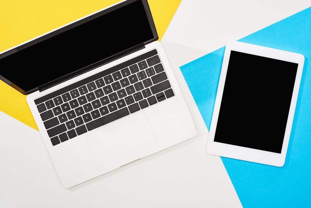 Draufsicht auf Laptop, digitales Tablet mit leerem Bildschirm auf gelbem, blauem und weißem Hintergrund - Foto, Bild