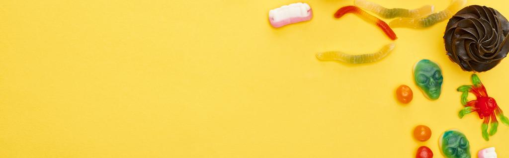 plano panorámico de coloridos dulces gomosos y cupcake sobre fondo amarillo, regalo de Halloween
 - Foto, imagen