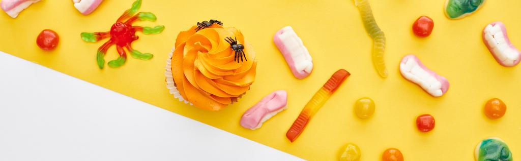 plan panoramique de bonbons gommeux colorés et cupcake sur fond jaune et blanc, festin d'Halloween
 - Photo, image