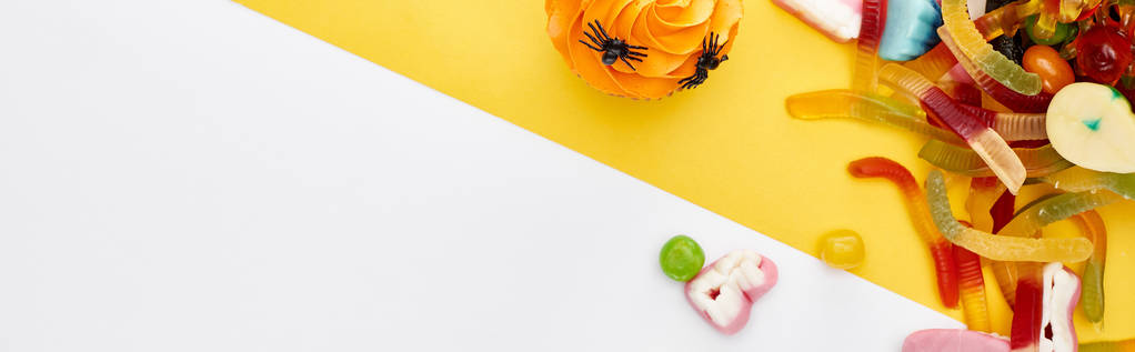 黄色と白の背景にカラフルなグミのお菓子やカップケーキのトップビュー, ハロウィーンの御馳走 - 写真・画像