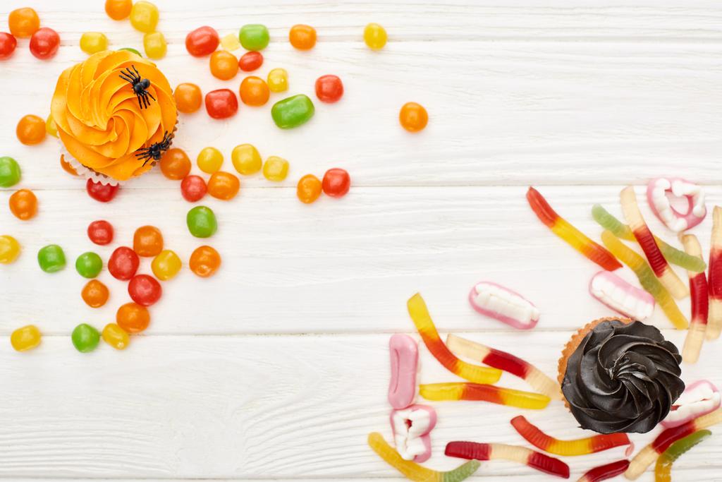 top view of colorful gummy sweets, cupcakes and bonbons on white wooden table, Halloween treat - Photo, Image