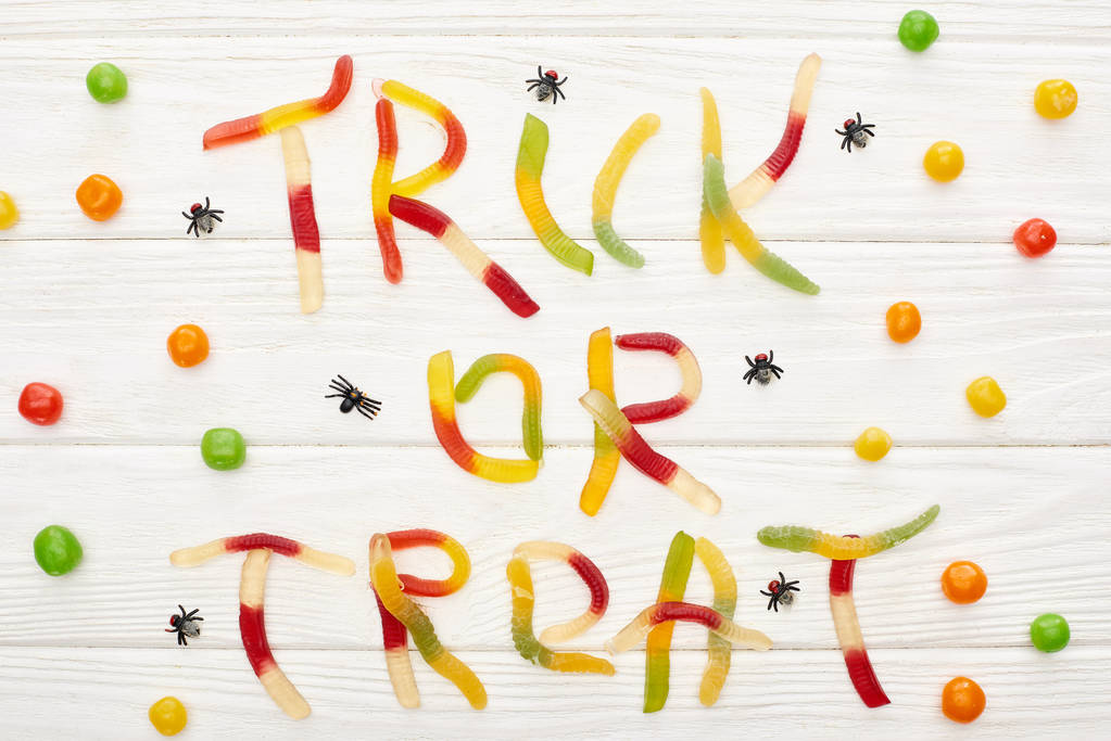 Widok z góry trick lub traktować napis wykonany z kolorowych gummy słodycze na białym drewnianym stole z pająkami i Bonbons, Halloween leczyć - Zdjęcie, obraz