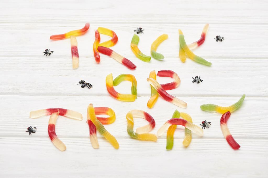 Nejlepší pohled na trik nebo na písmo z barevných gummých sladkostí na bílém dřevěném stole s pavouky, Halloween - Fotografie, Obrázek