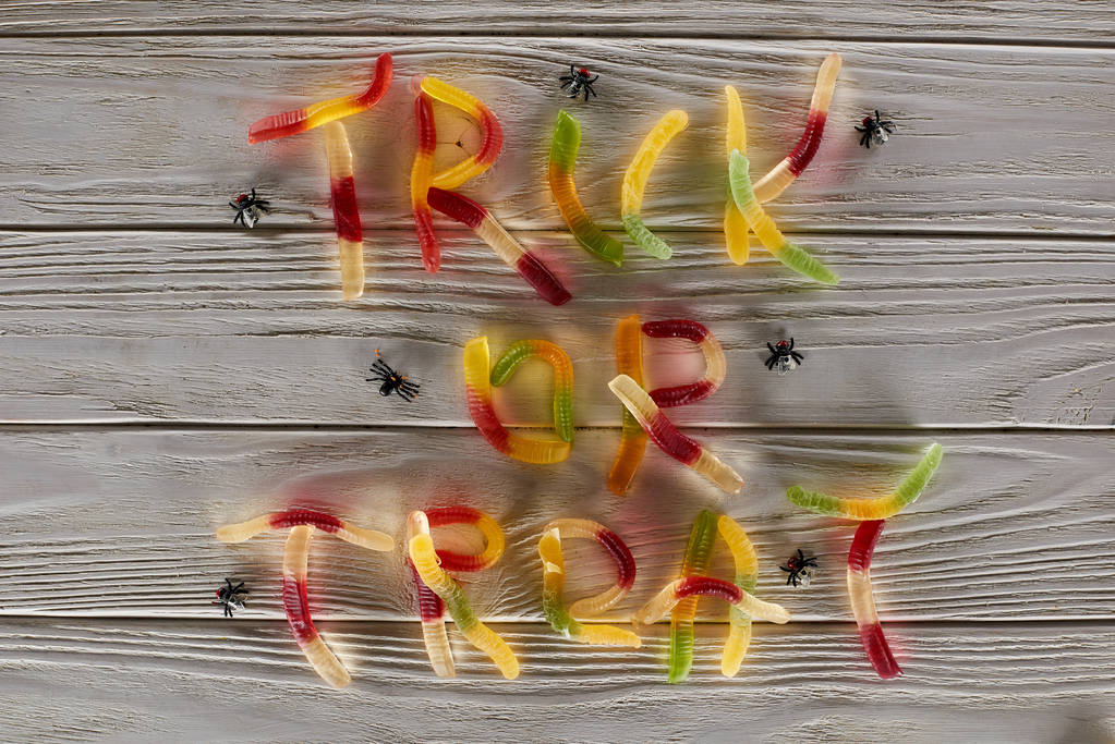 vista superior de truco o tratar letras hechas de dulces de goma de colores en la mesa de madera blanca con arañas, regalo de Halloween
 - Foto, imagen