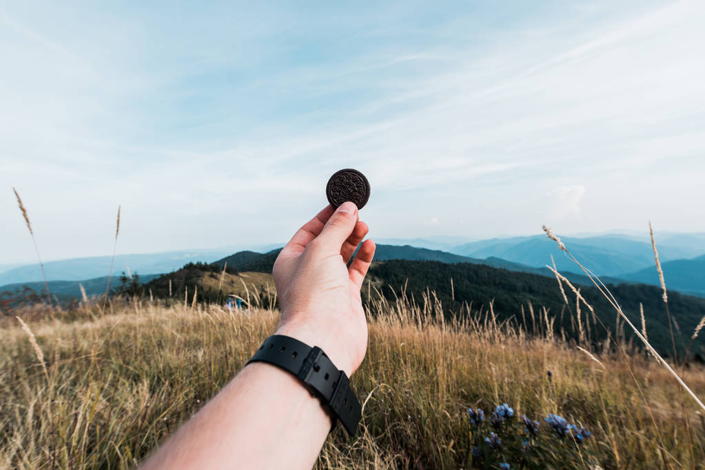 Карпати, Україна-24 серпня 2019: обрізаний вигляд людини тримає Oreo cookie в полі біля гір  - Фото, зображення