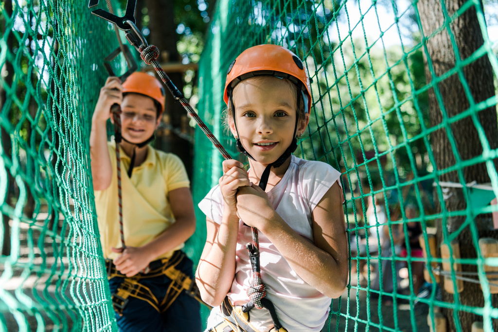 επιλεκτική εστίαση των ευτυχισμένων παιδιών σε κράνη με εξοπλισμό ύψους στο πάρκο περιπέτειας  - Φωτογραφία, εικόνα