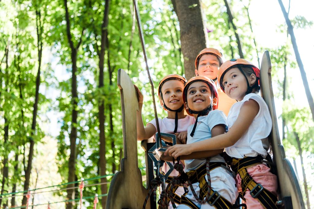 alegres niños multiculturales mirando hacia arriba en el parque de aventuras fuera
  - Foto, imagen