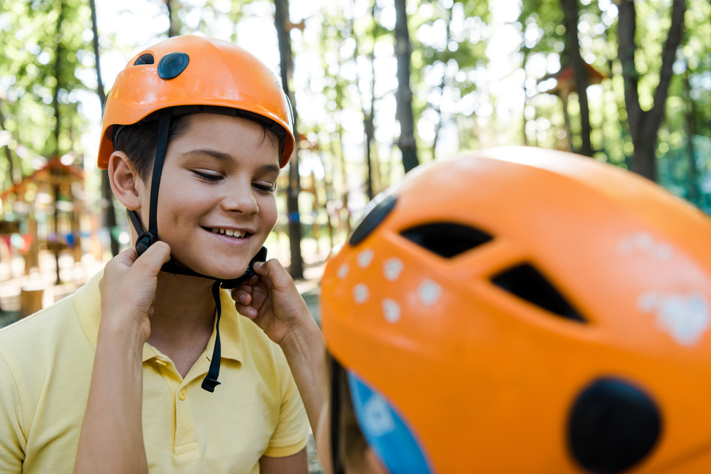 冒険公園で幸せな友人のヘルメットに触れる子供のクロップドビュー  - 写真・画像