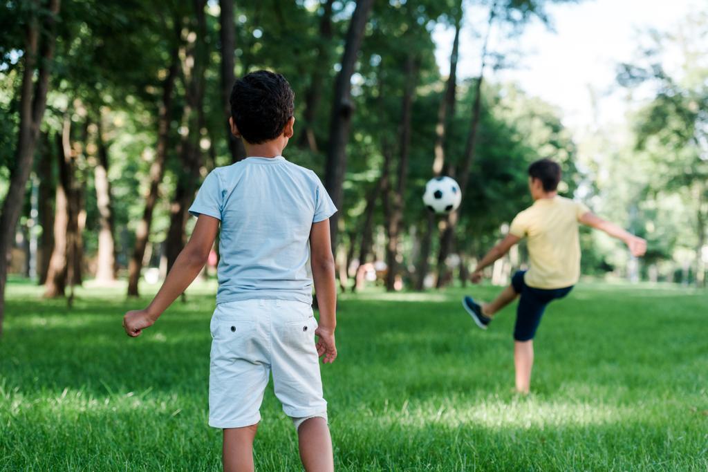 vista posterior del niño afroamericano de pie cerca de un niño jugando al fútbol
 - Foto, Imagen