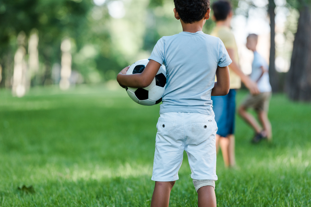 Rückansicht eines afrikanisch-amerikanischen Kindes, das mit Fußball neben Jungen steht  - Foto, Bild