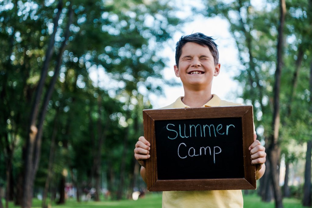 niño feliz con los ojos cerrados sosteniendo pizarra con las letras del campamento de verano
  - Foto, Imagen
