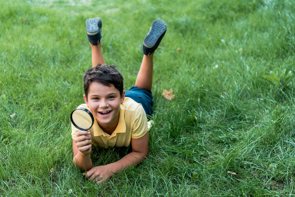 веселый мальчик лежит на траве и держа увеличитель
  - Фото, изображение