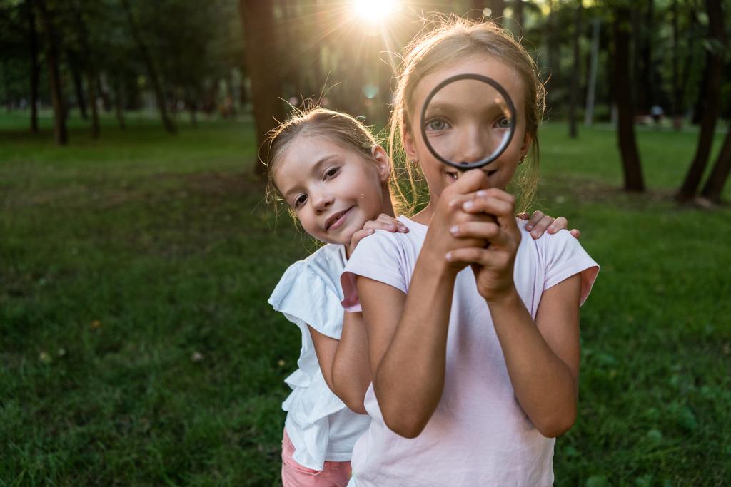 gelukkig kind houden vergrootglas in de buurt gezicht terwijl staan met een vriend in park  - Foto, afbeelding
