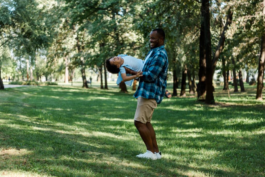 公園でかわいい息子を腕に抱いて幸せなアフリカ系アメリカ人の父親  - 写真・画像