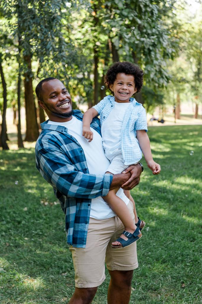 felice uomo africano americano in possesso di braccia carino bambino riccio
  - Foto, immagini