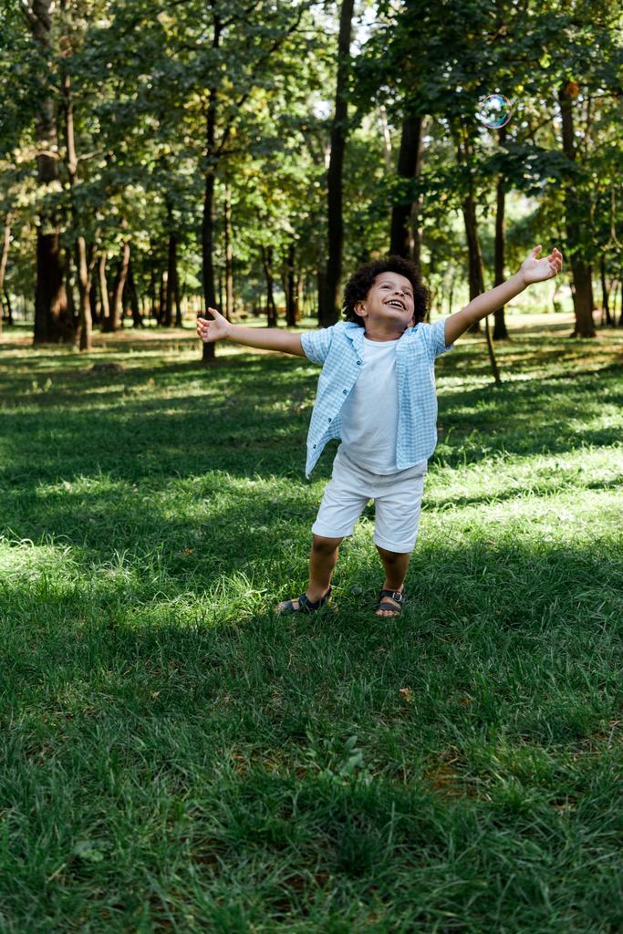 glückliches afrikanisch-amerikanisches Kind mit ausgestreckten Händen im Park  - Foto, Bild