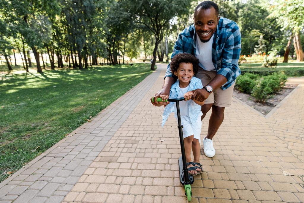 usmívající se africký Američan otec blízko roztomilým synem na skútru  - Fotografie, Obrázek