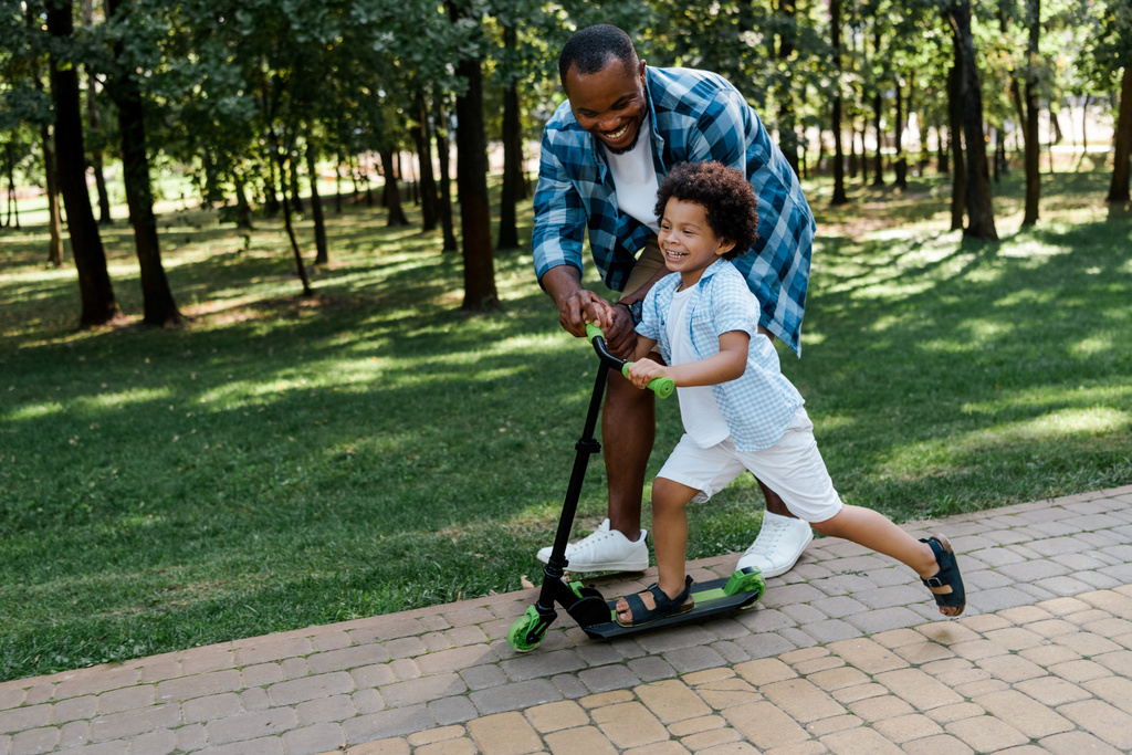 alegre pai americano africano perto criança feliz em scooter
  - Foto, Imagem
