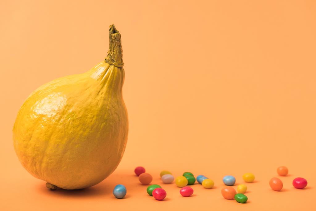 жовтий барвистий пофарбований гарбуз з цукерками на помаранчевому фоні
 - Фото, зображення