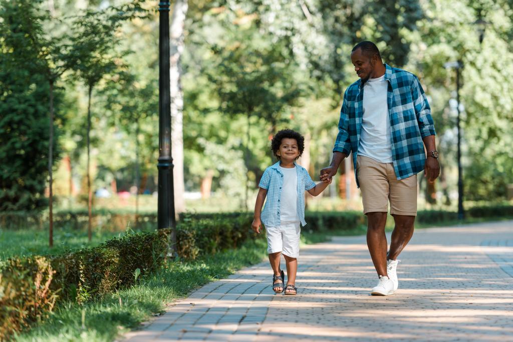 feliz afroamericano chico cogido de la mano mientras camina con padre
  - Foto, imagen