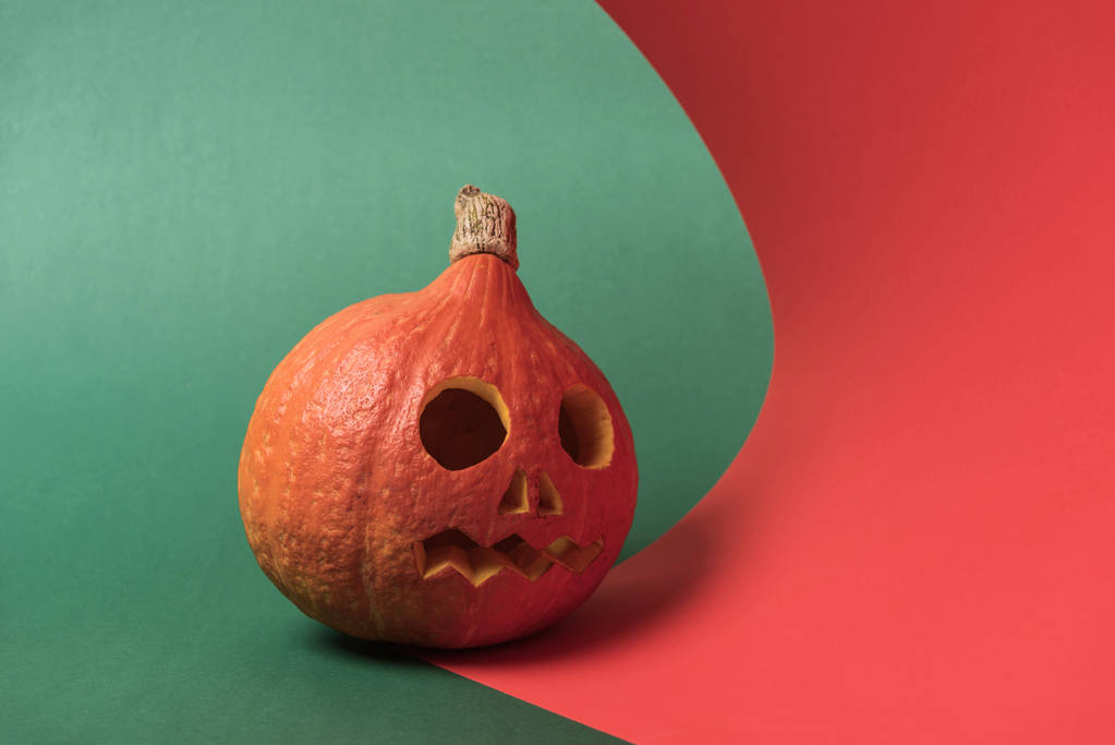 spooky carved Halloween pumpkin on red and green background - Photo, Image