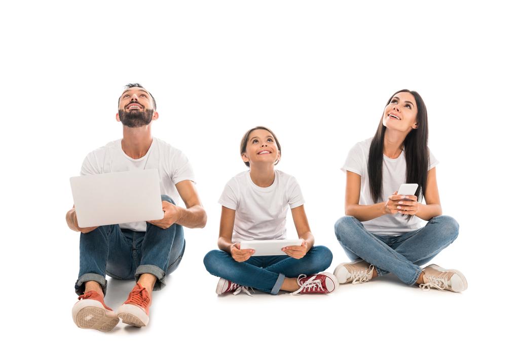 alegre familia sentada con gadgets y mirando hacia arriba aislado en blanco
  - Foto, imagen