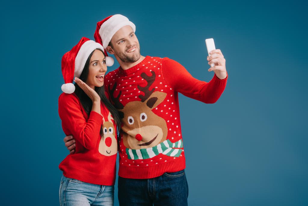 innoissaan pari santa hatut ja joulu villapaidat ottaen selfie älypuhelimeen eristetty sininen
 - Valokuva, kuva