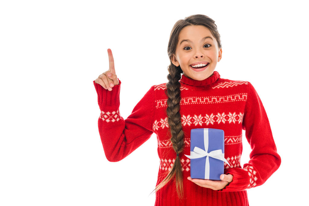 niño feliz en suéter sosteniendo presente y señalando con el dedo aislado en blanco
  - Foto, Imagen