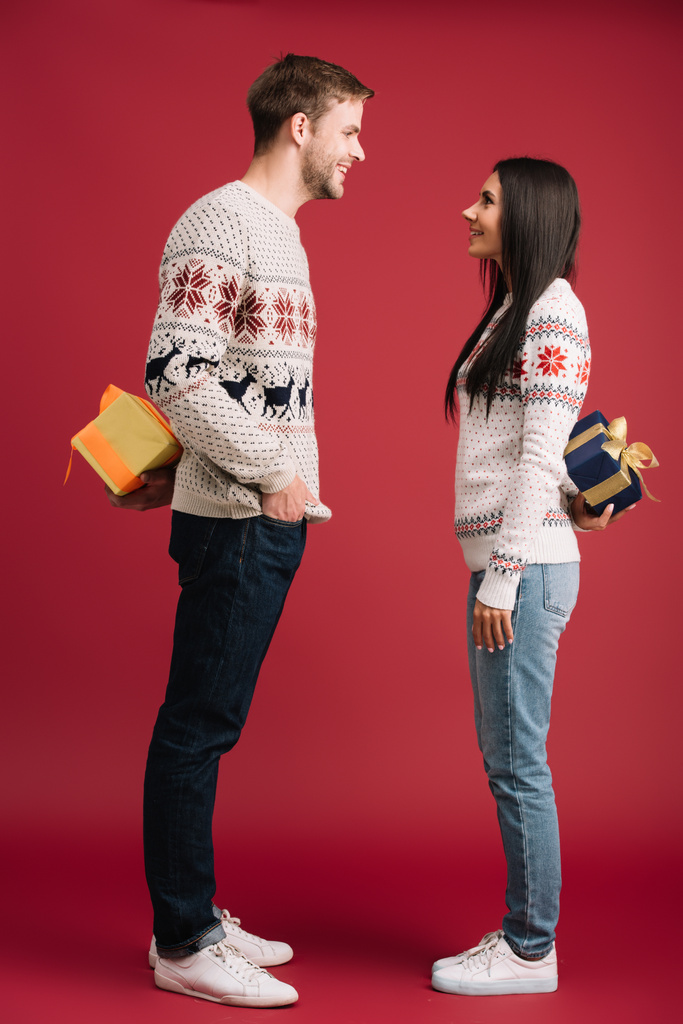 hermosa pareja ocultando cajas de regalo de Navidad aisladas en rojo
 - Foto, imagen