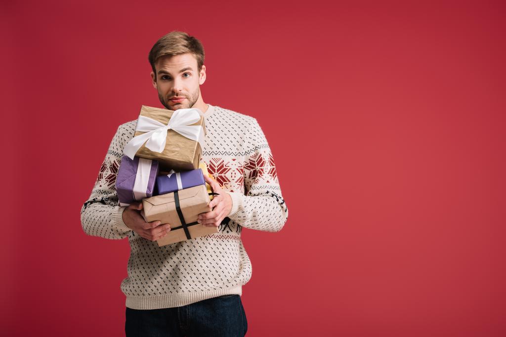 όμορφος νέος άντρας που κρατά Χριστουγεννιάτικα δώρα απομονωμένα στο κόκκινο - Φωτογραφία, εικόνα